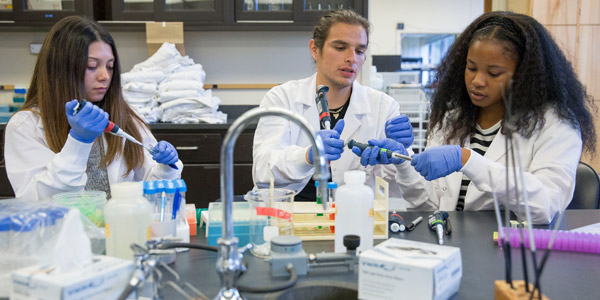 3 students in lab coats working in science lab