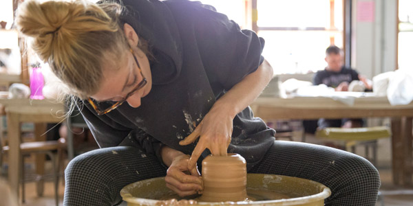 female student throwing a vessel on a pottery wheel